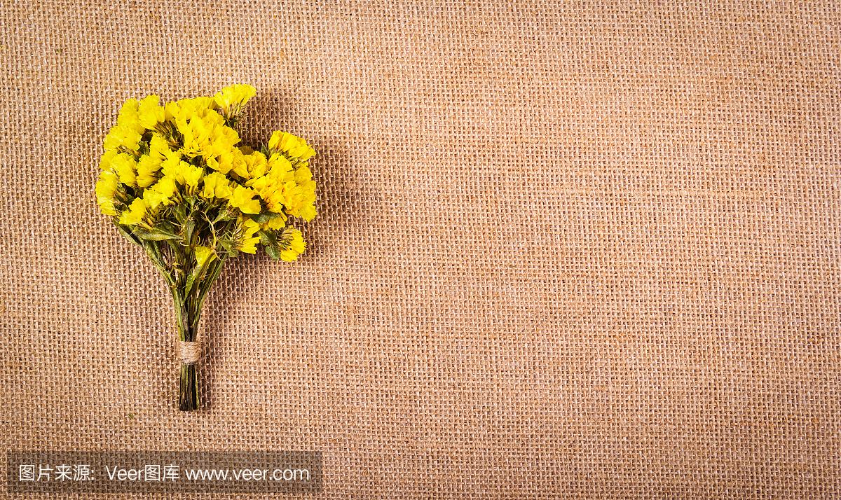 一束野花在麻袋的背景上。干的黄色花在天然亚麻的背景。